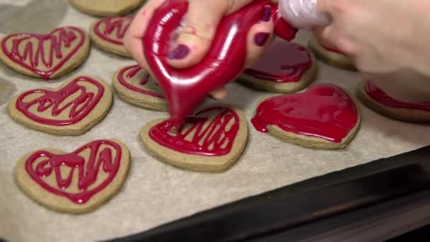 Zbliżenie ujęcia wyciskania czerwonego słodkiego lukru na ciasteczka w kształcie serca. Pieczenie ciasteczek na Walentynki — Wideo stockowe