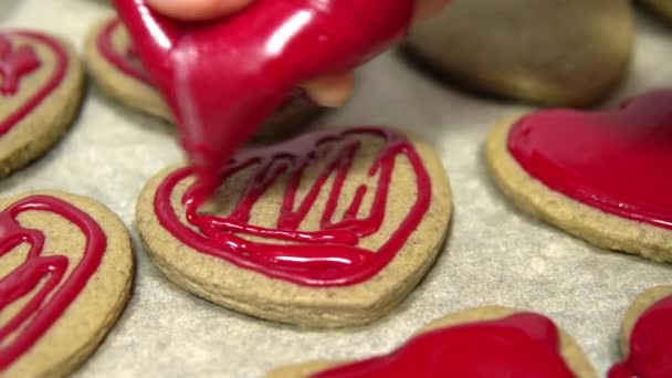 Zbliżenie ujęcia wyciskania czerwonego słodkiego lukru na ciasteczka w kształcie serca. Pieczenie ciasteczek na Walentynki — Wideo stockowe