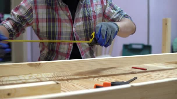 Um homem mede um pedaço de madeira com uma fita métrica. Um homem faz reparações em casa. Construtor, reparador com karashdash desenha no tabuleiro — Vídeo de Stock