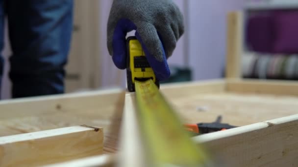 Un hombre mide un trozo de madera con una cinta métrica. Un hombre hace reparaciones en casa. — Vídeos de Stock