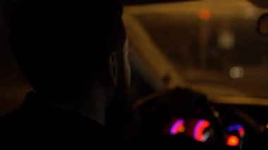 Sakallı bir adamın gece vakti yanan fenerlerin arka planına doğru araba sürüşü.