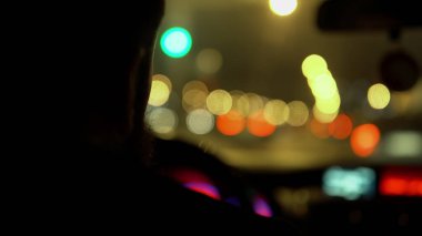 Sakallı bir adamın gece vakti yanan fenerlerin arka planına karşı araba sürüşü.