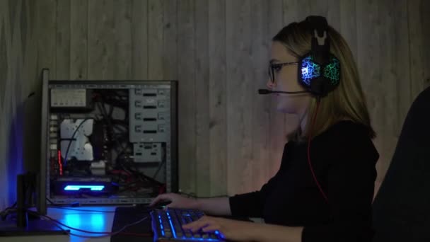 Девушка в наушниках играет в компьютерные игры и говорит в микрофон. Киберспортсмен дома — стоковое видео