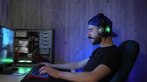Ένας μουσάτος τύπος με ακουστικά παίζει παιχνίδια στον υπολογιστή. Cybersportsman στο σπίτι Royalty Free Φωτογραφίες Αρχείου