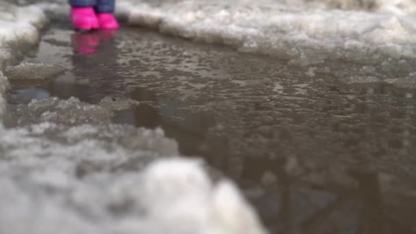 Dítě v růžových gumových botách kráčí v kaluži roztaveného sněhu. Jarní počasí — Stock video