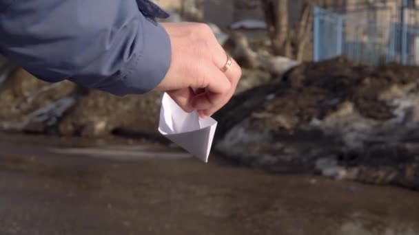 Une main adulte lance un bateau en papier blanc dans le courant d'eau de la neige fondante. Météo printanière — Video