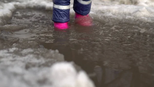 Dziecko w różowych gumowych butach chodzi w kałuży stopionego śniegu. Wiosenna pogoda — Zdjęcie stockowe