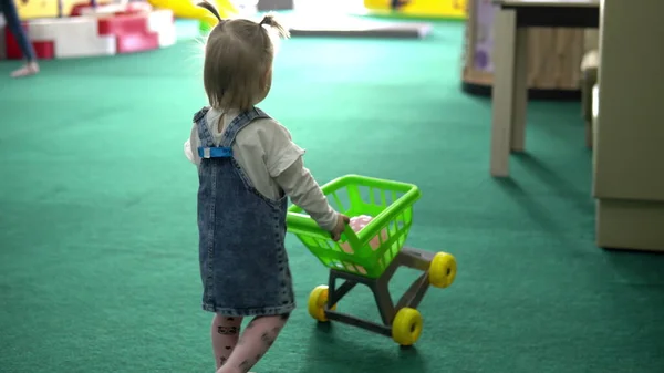 Pequena menina rolos brinquedo verde cesta de compras — Fotografia de Stock