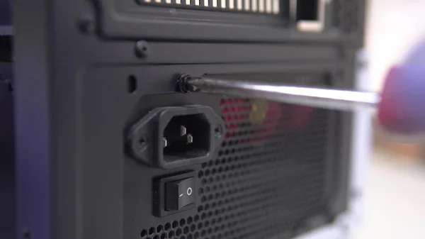 The repairman tightens the screw with a screwdriver into the PC power supply case. Home PC Maintenance and Upgrades