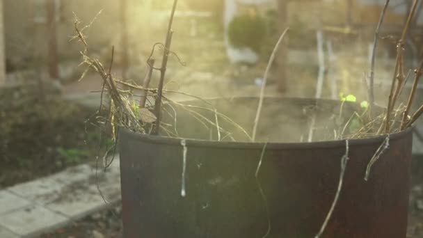 Metalen vat met afval erin. Rook komt uit het vat tegen de achtergrond van gele zonnestralen — Stockvideo