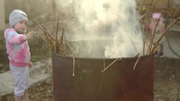 불타는 쓰레기로 통의 나뭇가지를 태우려고 하는 소녀 — 비디오