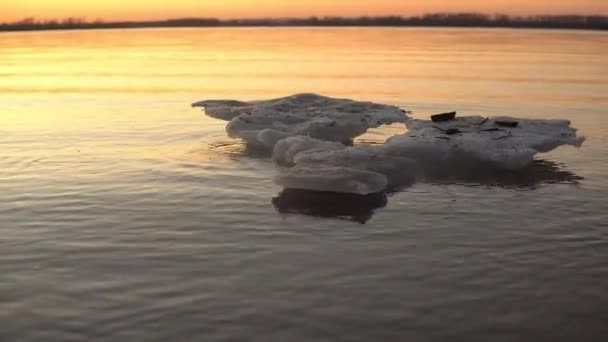 Un morceau de glace non fondue se trouve dans la rivière près du rivage sur fond de coucher de soleil — Video