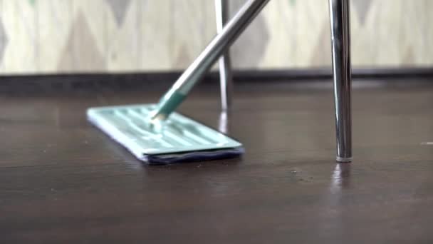 Girando in primo piano, la padrona di casa pulisce il pavimento vicino alla gamba sotto la sedia — Video Stock