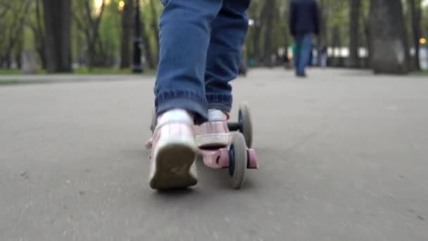 Une fille dans le parc monte un scooter à trois roues sur l'asphalte — Video