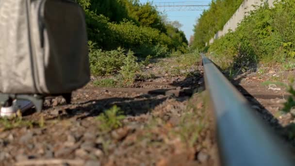 En kvinna med en resväska i handen går längs sömnen. Res på järnvägsspår. Gamla tågspår — Stockvideo