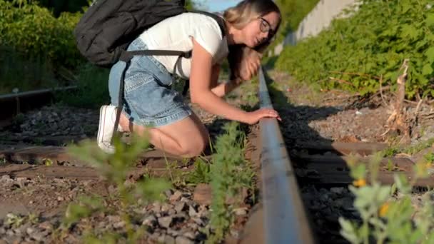 Una mujer con una mochila en la espalda pone su oído en las vías del tren. Viajar por los ferrocarriles. Vía férrea — Vídeos de Stock