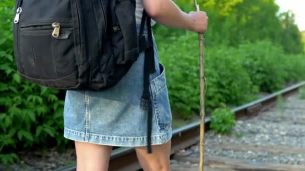 Una chica con una mochila y un palo en la mano camina a lo largo de los durmientes. Viaja por las vías del tren. Vía férrea — Vídeos de Stock