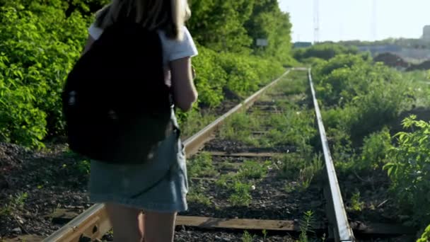 Una ragazza con uno zaino cammina lungo le traverse. Viaggiare su binari ferroviari. Vecchio binario del treno — Video Stock
