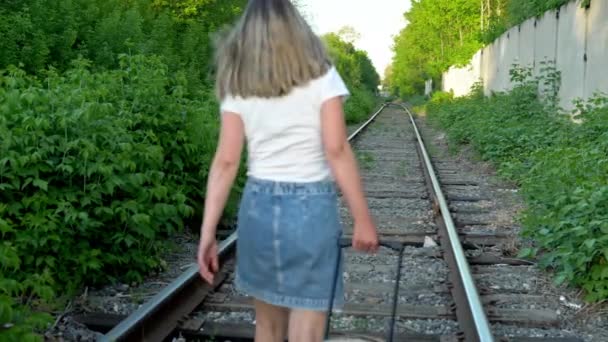 A woman walks along the sleepers and carries a suitcase behind her. Travel on railroad tracks. Old train track — Stock Video