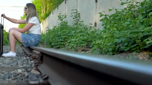 Kvinnan satte sig på rälsen och höll i en resväska. Res på järnvägsspår. Gamla tågspår — Stockvideo