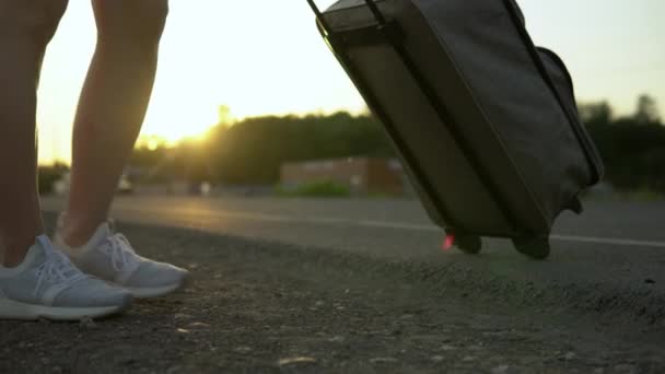 Жінка стоїть вздовж траси з валізою. Автостоп. Крупним планом жіночі ноги — стокове відео