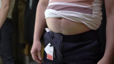 Koca göbekli bir adam soyunma odasında pantolon deniyor ve düğmelerini ilikleyemiyor.