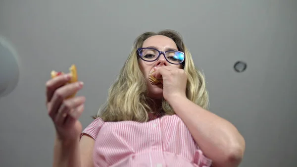 Het meisje kruipt op de weegschaal met cupcakes in haar handen en eet ze op. Wegen op weegschalen. Sluiten van gewichtsverlies controle. Meting van overgewicht. — Stockfoto