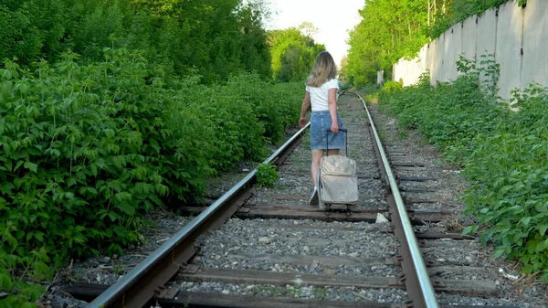 Bir kadın pusucular boyunca yürür ve arkasında bir bavul taşır. Demiryolu raylarında seyahat et. Eski tren yolu — Stok fotoğraf