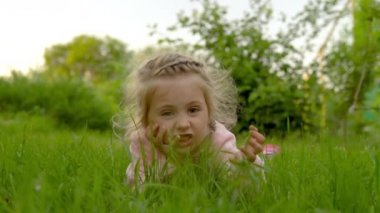 Çimenlerde yatan ve yüzünü buruşturan bir kız. Yazın tatmin olmuş bir çocuk. 4k