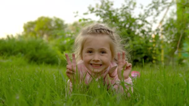 Chica acostada en la hierba agitando sus manos. Niño satisfecho en el verano. 4k — Vídeos de Stock