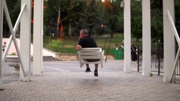 Un vecchio solitario che dondola su un'altalena nel parco. Una persona che riposa nel parco 4k — Video Stock