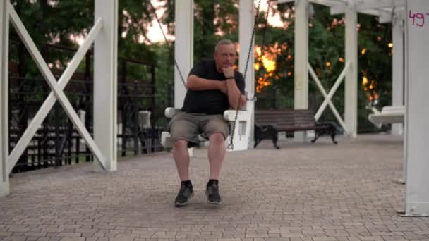 Одинокий старик качается на качелях в парке. Один отдыхающий в парке 4k — стоковое видео