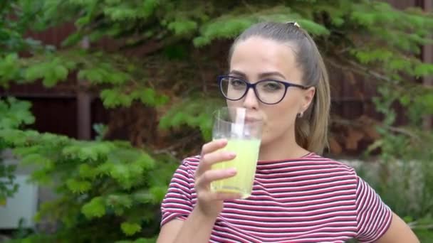 Девушка в очках держит стакан с витаминным напитком в руке и пьет его. Поддержание иммунитета. Здоровый образ жизни. 4k — стоковое видео
