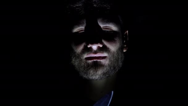 Cechy męskiej, brodatej twarzy, podświetlanej w ciemności. Zbliżenie twarzy mężczyzny w ciemności, który trzyma nóż w ręku — Wideo stockowe