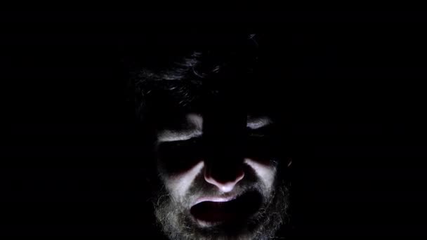 Caracteristici ale unei fețe supraaglomerate de sex masculin, iluminată din spate în întuneric. Închideți fața unui om în întuneric care își deschide gura — Videoclip de stoc