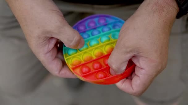 Een oude man speelt in een pop close-up. De persoon is gepassioneerd door regenboog anti-stress. Speelgoed van kindersiliconen — Stockvideo