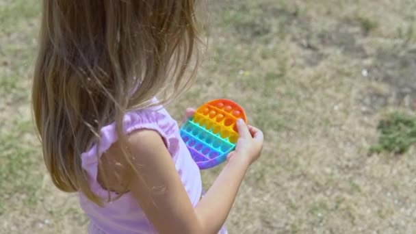 La chica de rosa juega al popit. El niño es apasionado por el arco iris anti-estrés. Juguete de silicona para niños — Vídeos de Stock