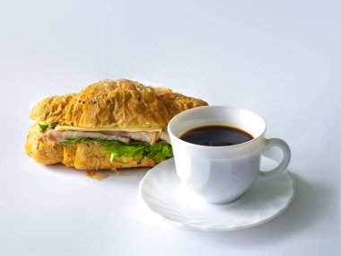 Etli, peynirli, sebzeli ve beyaz fincanlı kruvasan sandviçi.