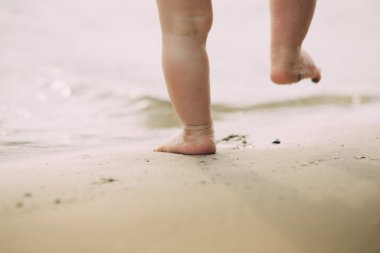 Toddler bebek ilk adımlarını banka yakınındaki kum üzerinde yapıyor 