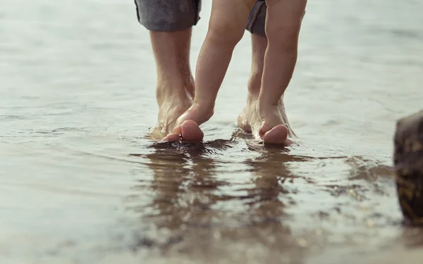 Pieds nus père et son petit fils restant dans l'eau réfléchissante — Photo