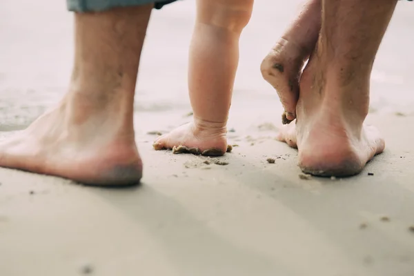Γυμνά πόδια πατέρα και τον μικρό γιο που διαμένουν στην άμμο κοντά στο νερό — Φωτογραφία Αρχείου