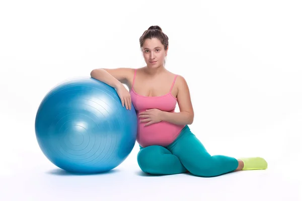 Mladá těhotná žena v jasném sportovním oblečení sedí v blízkosti velkého modrého míčku pro fitness — Stock fotografie