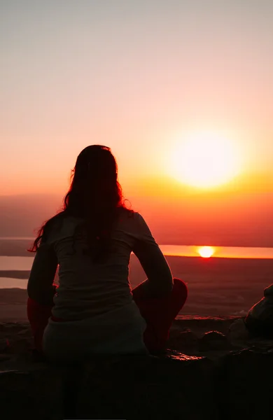 Sylwetki kobieta siedzi na ziemi i patrząc na zachód słońca — Zdjęcie stockowe