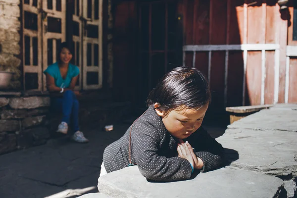 Nepalee child from the village praying and his mother looking at him from the backside of the yard of their house — Stock Photo, Image