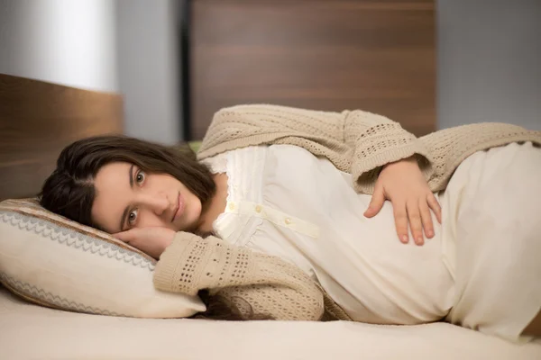 Mujer embarazada en ropa de casa acostada en la almohada en el dormitorio con muebles modernos — Foto de Stock