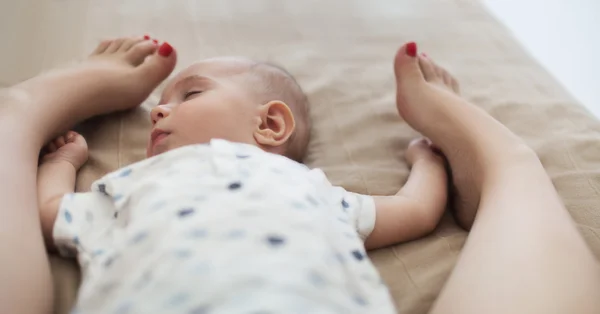 Little beautiful toddler slipping holding mother's legs — Stock Photo, Image