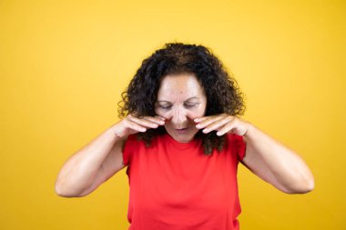 Orta yaşlı bir kadın, günlük gömleğini giymiş, sarı arka planda durmuş, elleri ağızda bağırıyor ve bağırıyordu.