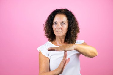 Normal beyaz gömlek giyen orta yaşlı bir kadın soyutlanmış pembe arka planda duruyor. Elleriyle jest yapıyor, hayal kırıklığına uğramış ve ciddi bir yüz ifadesi takınıyor.