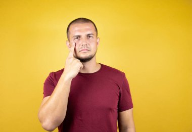 Rus adam, sarı tişörtlü, özgün kırmızı tişörtlü. Gözünü dikip jestini izliyor. Şüpheli bir ifade.