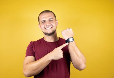 Rus adam sarı üzerine kırmızı tişört giymiş. İzole edilmiş arka plan şaşırmış ve saatini göstermiş. Çünkü geç olmuş.